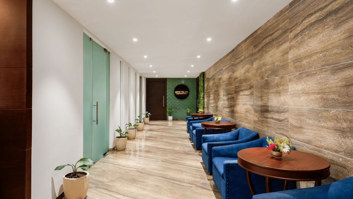 Tables and seaters placed against a patterned wall with planters opposite to them and the logo of Spectrum in the background at Voyage Milestone Hotel And Banquet 